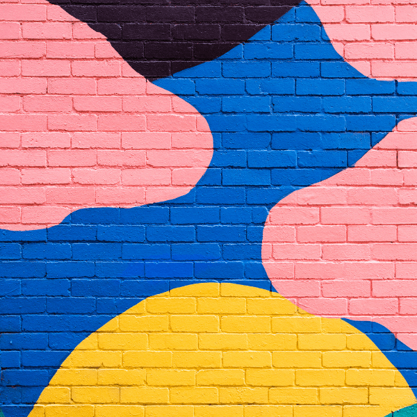 Colorful abstract mural on a brick wall with pink, blue, and yellow shapes.